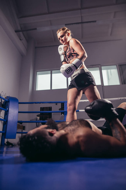 low angle view of woman boxer celebrating victory while man lying on ring floor - Fotó, kép