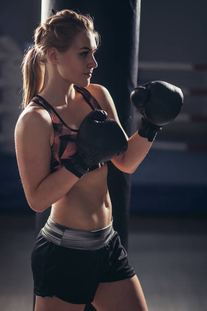 Female Boxer wearing gloves posing in boxing studio - Foto, immagini