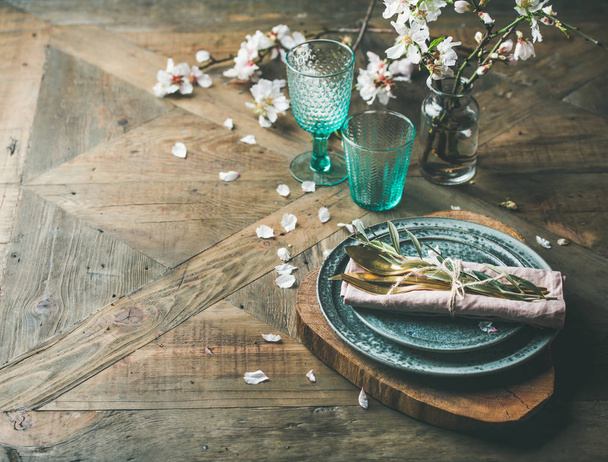 Spring Easter holiday Table setting. Tender almond blossom flowers on branches, plates, glasses and cutlery over vintage wooden table - Foto, imagen