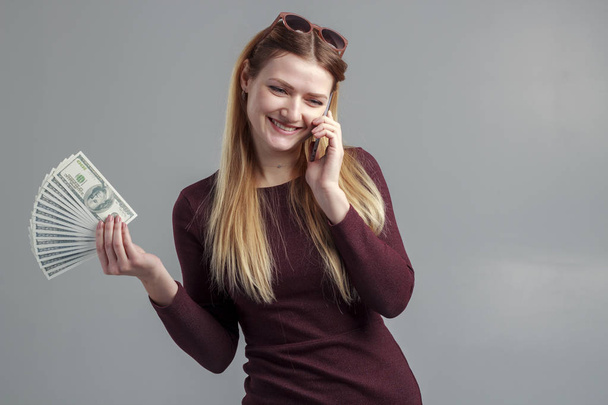 Η εικόνα ενός κοριτσιού επιχειρήσεων, κερδίζουν από το τηλέφωνο. Μια ισχυρή ανεξάρτητη γυναίκα μιλάει στο τηλέφωνο με χρήματα στα χέρια της. - Φωτογραφία, εικόνα