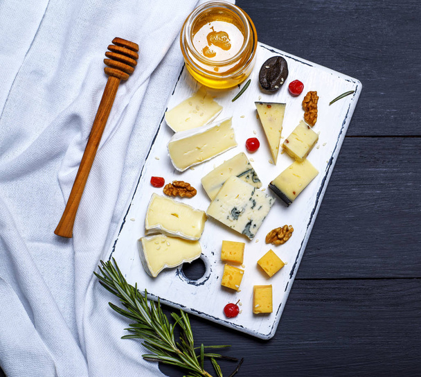 Käsestücke auf weißem Brett und ein Glas mit Honig - Foto, Bild