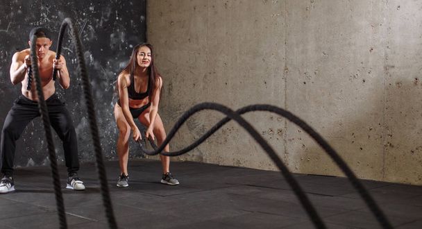Woman and man couple training together doing battling rope workout - Foto, imagen
