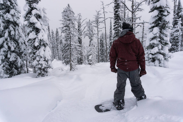 Hombre snowboarder de pie y mirando las empinadas laderas nevadas antes de montar. Tomado en Whitewater Ski Mountain, Nelson, Columbia Británica, Canadá
. - Foto, Imagen