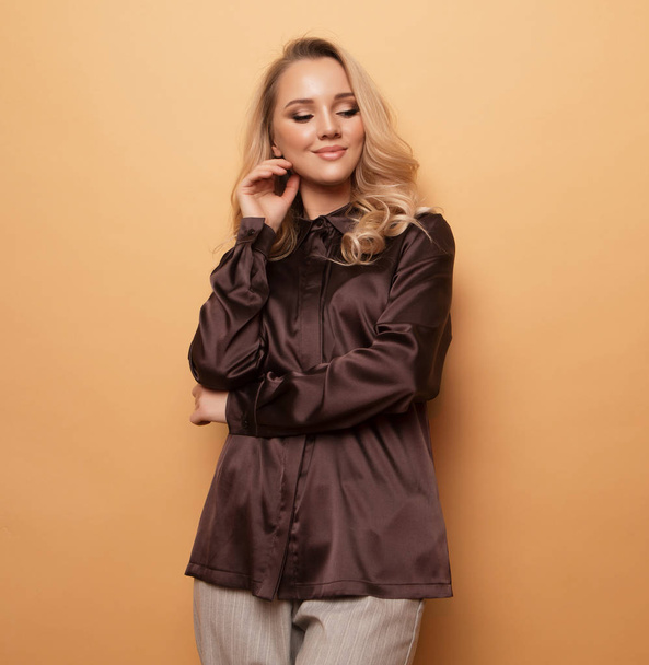 Stylish blond woman in blouse and pants posing on beige background. - Photo, image