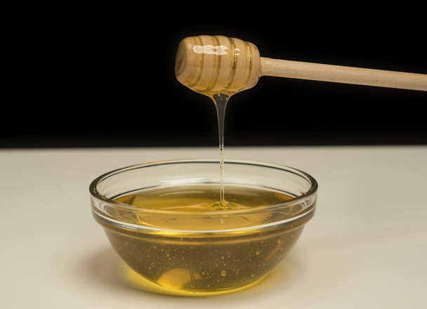 Miel dorada natural que brota de un rociador de madera sobre fondo negro
 - Foto, Imagen