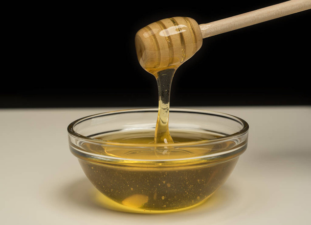 Natural golden honey oozing from a wooden drizzler on black background - Photo, Image