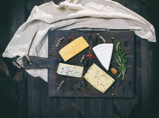 pieces of different cheeses on a brown wooden board - Foto, Imagem