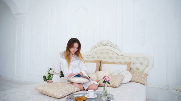 Huisvrouw bladeren door pagina's van Magazine en lees nieuws, zittend op grote Bed - Foto, afbeelding