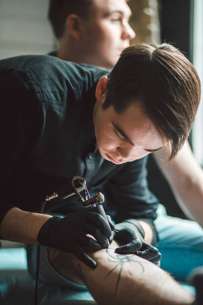 tattoo male artist makes a tattoo on a female leg. - Фото, зображення
