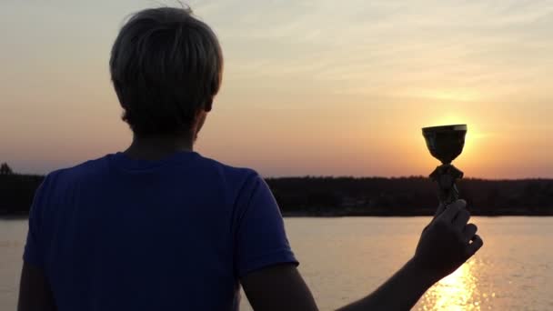 Glücklicher Mann hält seine Siegerschale auf einem Sonnenweg am See - Filmmaterial, Video