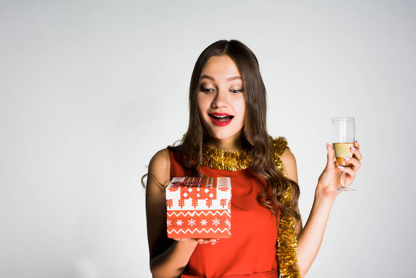 happy young girl in red dress celebrates the new year, holds a glass of champagne and a gift - 写真・画像