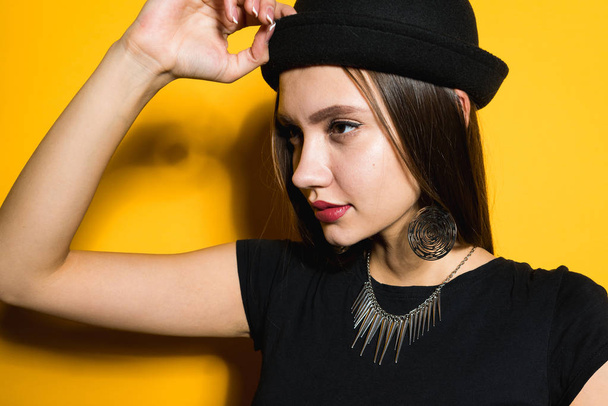stylish confident girl in a black dress and a fashionable hat posing on a yellow background, expensive jewelry - Foto, Imagem