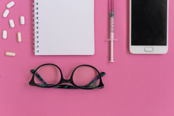 on a pink background lies a pill, notepad, glasses, phone - Φωτογραφία, εικόνα