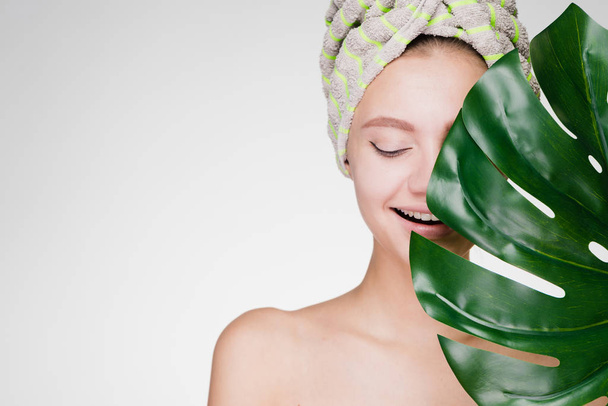 young happy girl with a towel on her head holds a green leaf in her hands, enjoying spa treatments - Photo, image