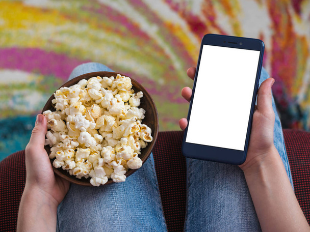 Girl holding a phone with clipping white background. A bowl of popcorn on the child's lap. - Photo, Image