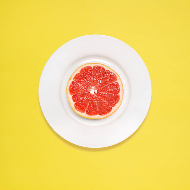 Red grapefruit slice on white plate on yellow background. - Φωτογραφία, εικόνα