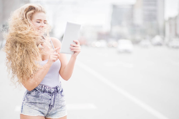 Happy young woman with vintage music headphones around her neck, surfing internet on a tablet pc and posing against urban city background. - Foto, Imagem