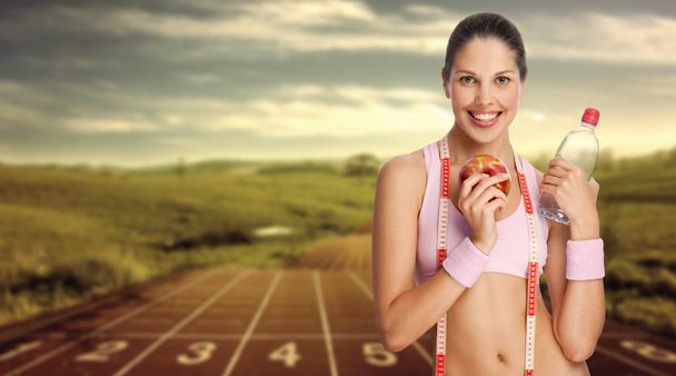 Una joven atlética sosteniendo agua y manzana contra pista de atletismo
. - Foto, imagen