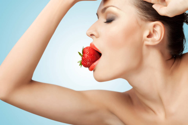 A portrait of a nude sexy woman holding a red-ripe strawberry in her mouth. - Foto, imagen