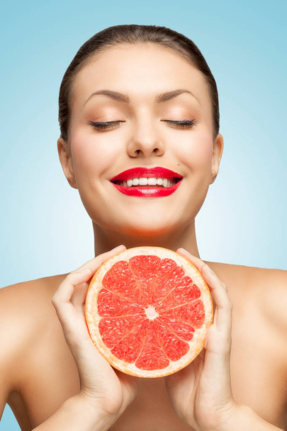 A creative portrait of a beautiful smiling woman squeezing a red grapefruit in her hands. - Foto, Bild
