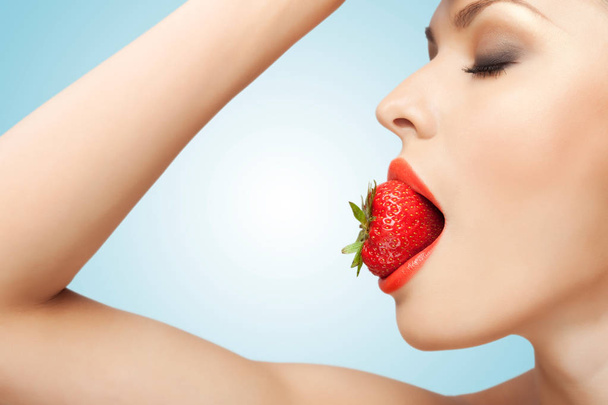Un retrato de una mujer sexy desnuda sosteniendo una fresa roja madura en su boca
. - Foto, imagen