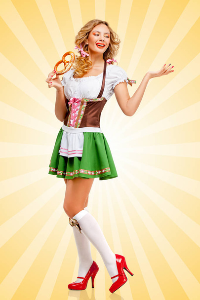 Beautiful sexy Oktoberfest woman wearing a traditional Bavarian dress dirndl posing with a soft salty pretzel on colorful abstract cartoon style background. - Foto, imagen