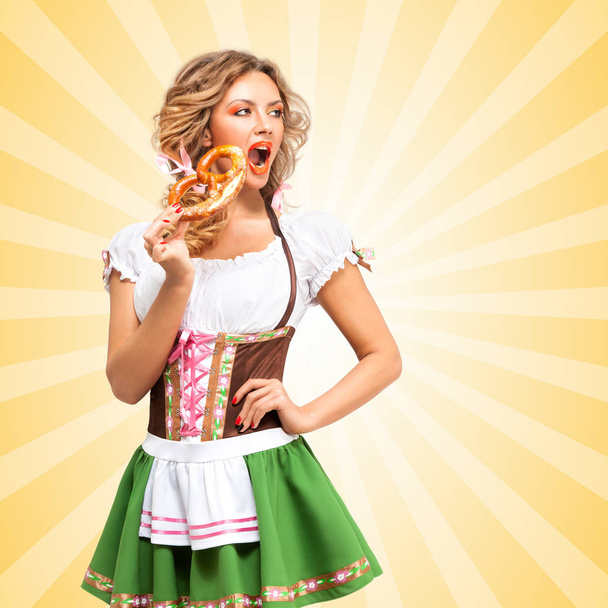 Beautiful sexy Oktoberfest woman wearing a traditional Bavarian dress dirndl with open mouth eating a pretzel on colorful abstract cartoon style background. - Foto, imagen