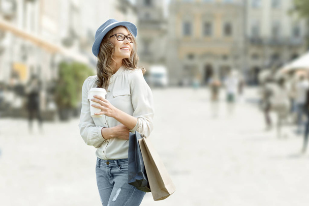 Onnellinen nuori muodikas nainen ostoskassit nauttia kahvin jälkeen ostoksia ja tilalla ottaa pois kahvia vastaan kaupunkien tausta
. - Valokuva, kuva