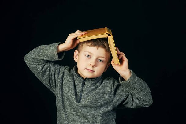 Menino cansado segurando um livro sobre sua cabeça.O conceito de educação pré-escolar
 - Foto, Imagem