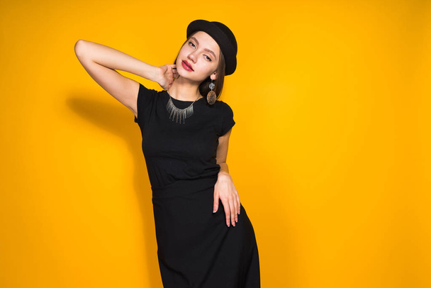 attractive luxury girl in a black dress and a fashionable hat posing, on the neck an expensive necklace - Фото, изображение