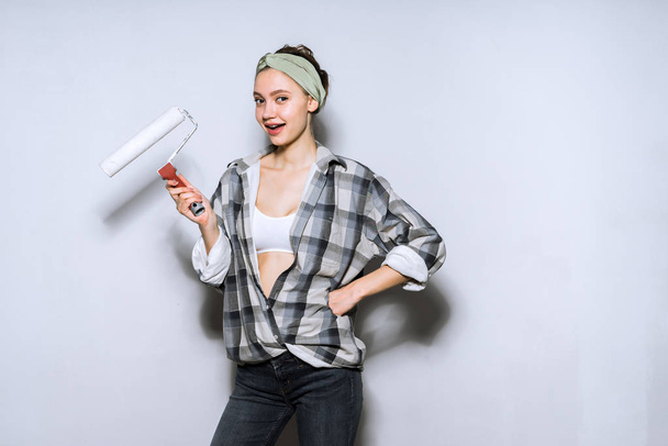 cute beautiful girl painter holding in his hand roller for painting walls, white paint, repair in apartment - Fotoğraf, Görsel