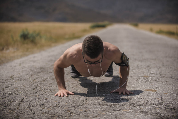 Corredor masculino haciendo flexiones en la carretera de montaña bajo el sol concepto de estilo de vida saludable - Foto, Imagen