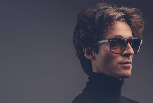 Studio portret zmysłowy męskiego macho z stylowe włosów w czarny sweter i okulary przeciwsłoneczne. - Zdjęcie, obraz