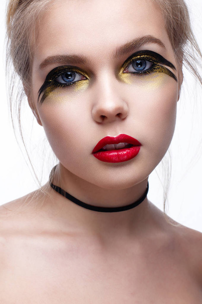 Young girl with creative black and gold makeup. Beautiful model with a checker on the neck and red lips. Perfect skin. Beauty of the face. Photo is taken in the studio. White isolated background. - Photo, Image