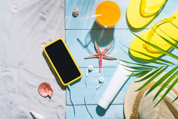 Letnie wakacje. Żółte klapki, słomkowy kapelusz, sok pomarańczowy i telefonu komórkowego - Zdjęcie, obraz