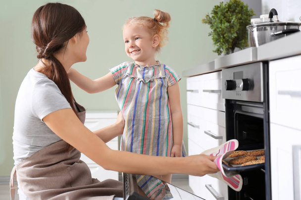 Little girl watching her mother bake cookies in oven indoors - 写真・画像