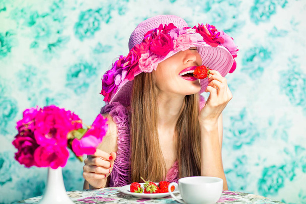 Beautiful girl in pink dress over floral vintage blue background. Art work of romantic woman. Pretty tender spring woman eat strawberry - Photo, Image