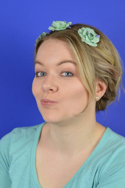 portrét skeptické mladé blonďaté běločké ženy s vlasy a azurovou kyticí na vlasech před modrým pozadím - Fotografie, Obrázek