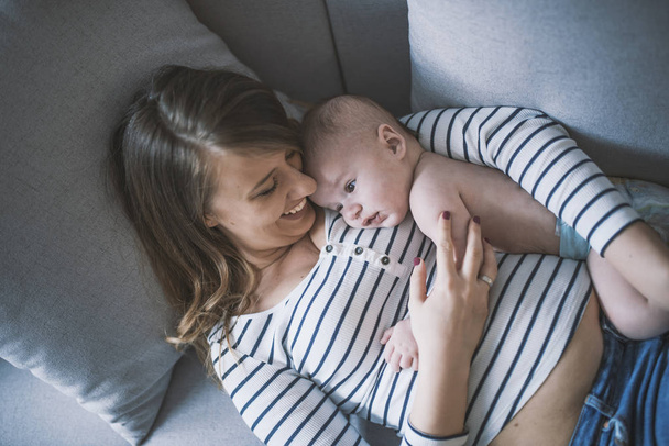Young mother holding her newborn child. Woman and new born boy relax. Family at home. Portrait of happy mother and baby. Young beautiful mom lying at bed with a cute little child. - Foto, imagen