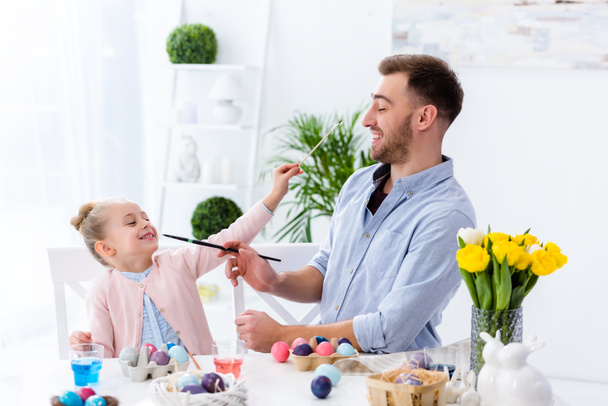 Father and daughter having fun while painting eggs for Easter - Foto, Bild