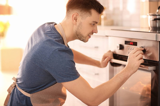Man adjusting electric oven in kitchen - Fotoğraf, Görsel