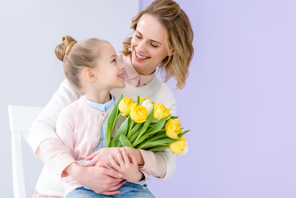Cute child embracing mother with tulips bouquet on 8 march - Photo, Image