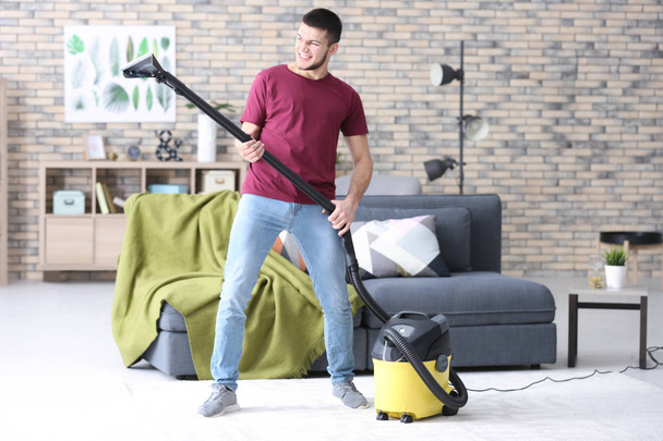 Young man hoovering floor while cleaning flat - Fotografie, Obrázek