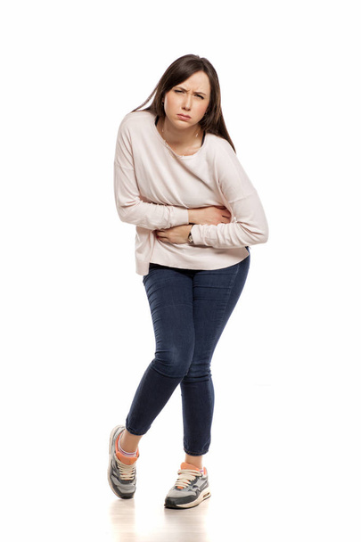 Jonge vrouw met maagpijn op een witte achtergrond - Foto, afbeelding