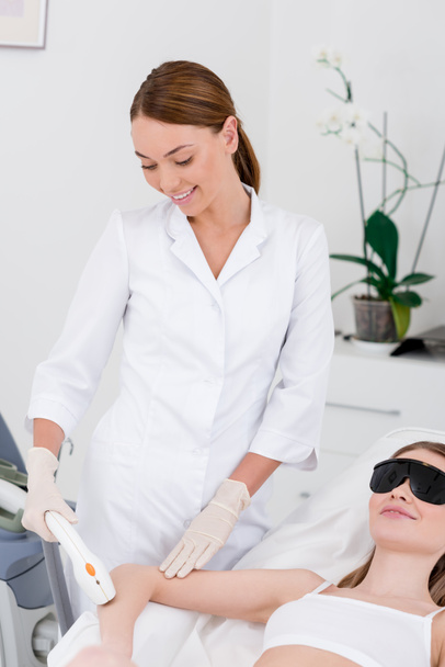 woman receiving laser hair removal procedure on arm made by cosmetologist in salon - Photo, Image
