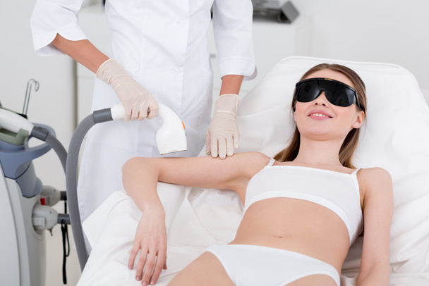 częściowy widok kobieta odbiera zabiegiem depilacji laserowej na ramię wykonana przez kosmetyczki w salonie - Zdjęcie, obraz