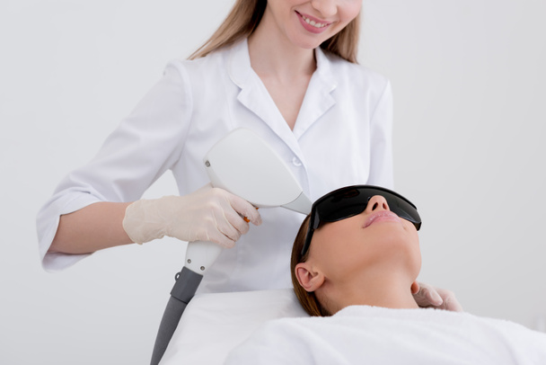 partial view of young woman receiving laser hair removal epilation on face in salon - Foto, Bild
