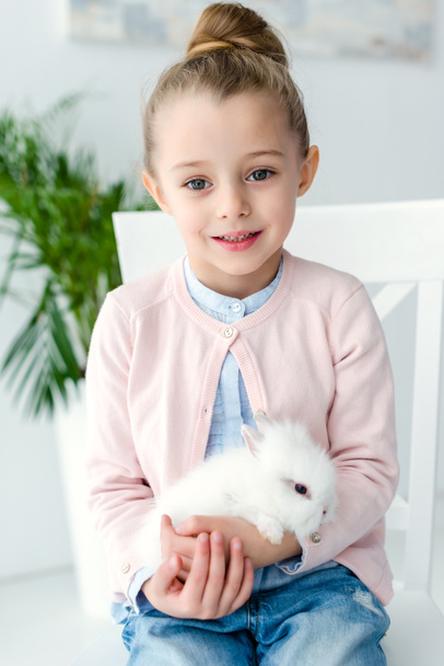 Λευκό κουνέλι κάθεται στα γόνατα του παιδιού κορίτσι - Φωτογραφία, εικόνα