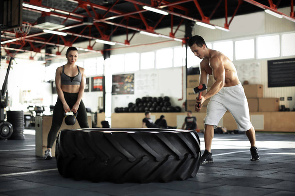 Young muscular man hitting heavy tire with hammer in gym - Foto, immagini
