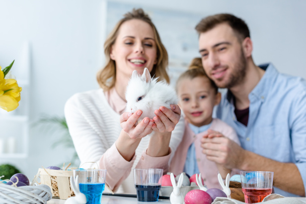 Mother with family holding cute bunny by table with Easter eggs - 写真・画像
